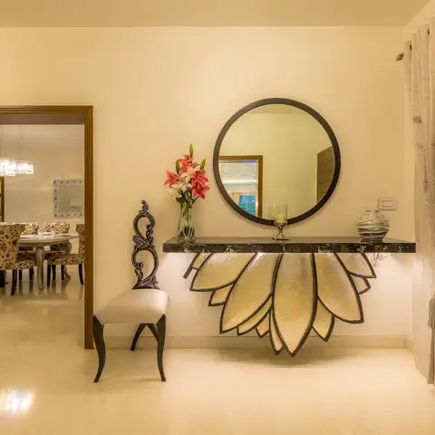 Entrance foyer with a sculptural gold lotus-petal console table beneath a round black-framed mirror, a carved baroque-style accent chair