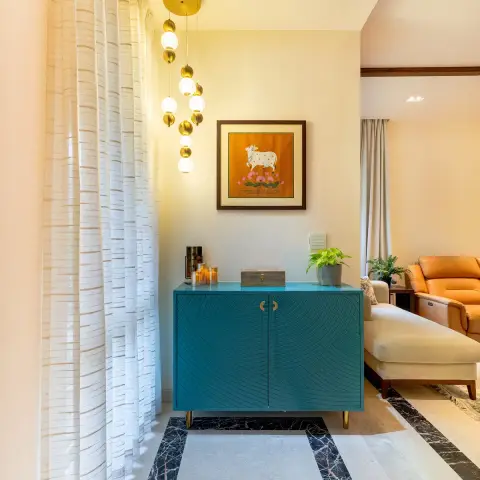 Entrance foyer with a teal sunburst-grooved cabinet on brass legs, a framed Pichwai cow painting above it