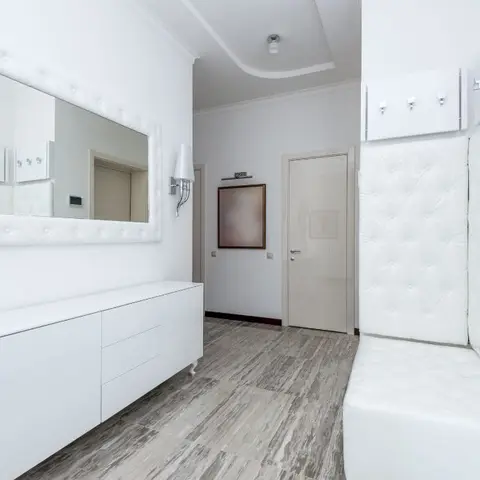 Entrance foyer with a tufted white bench and matching wall panel, a floating white console beneath a tufted-frame mirror, and crystal wall sconces