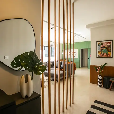 Entrance foyer with a vertical wood-slat jaali screen framing the living room beyond, a round mirror and sculptural vase on a console