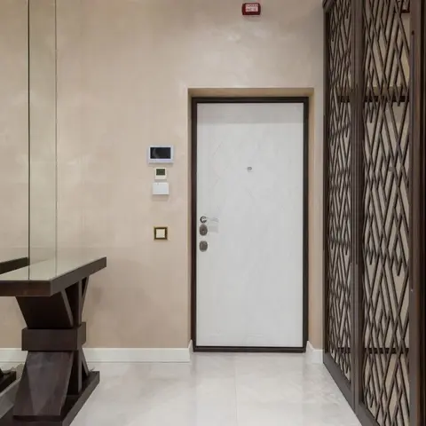 Entrance foyer with a white panelled main door beside a dark wood diamond-lattice jaali partition and a mirrored console table.