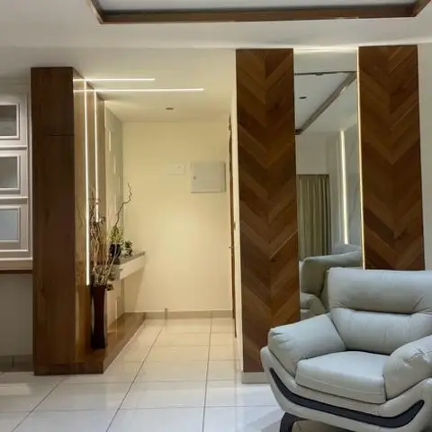 Entrance foyer with chevron wood-panelled pillars flanking a full-height mirror and a grey leather armchair on white tile flooring.