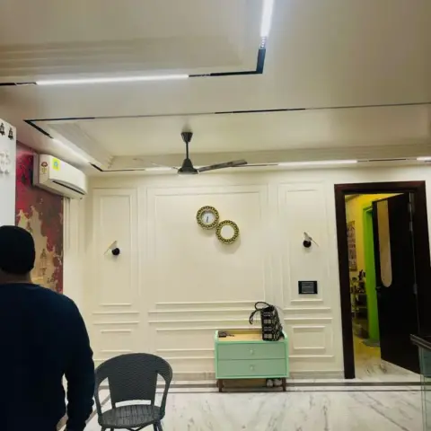 Entrance foyer with raised-panel wall moulding, a stepped POP ceiling traced in linear LED lighting, matching wall clocks