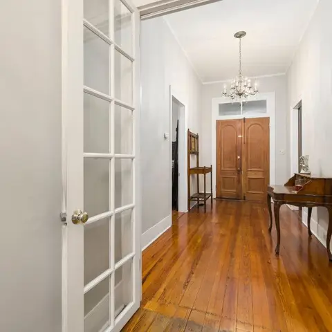 Entrance hallway leading to a panelled wood front door, with a mini chandelier overhead and a carved console table against the wall