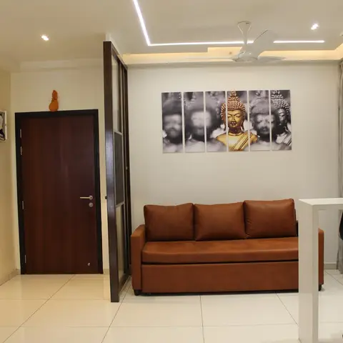 Entrance hallway opening into a living area with a tan leather sofa beneath a six-panel Buddha photographic wall art, cove-lit ceiling