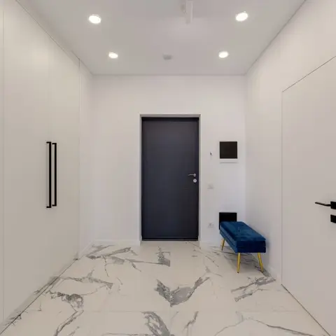 Entrance hallway with a charcoal flush main door, book-matched white marble flooring, a full-height white wardrobe wall