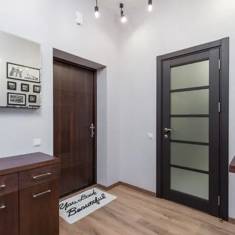 Entrance hallway with a dark wood front door, a frosted-glass internal door, a wall mirror above a wood storage console, and a gallery of small photo frames.