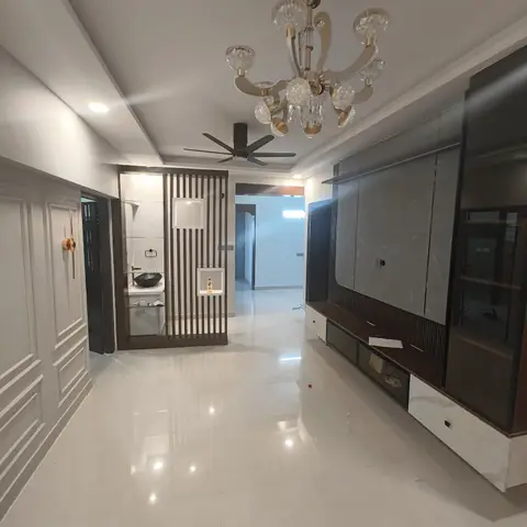 Entrance hallway with a fluted wood partition screen beside a small wash counter, opening onto a living room with a grey marble-clad TV wall under a crystal