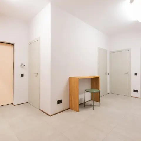 Entrance hallway with a peach-toned main door, wall-mounted wood coat pegs, and a slim wood console table paired with a green stool.