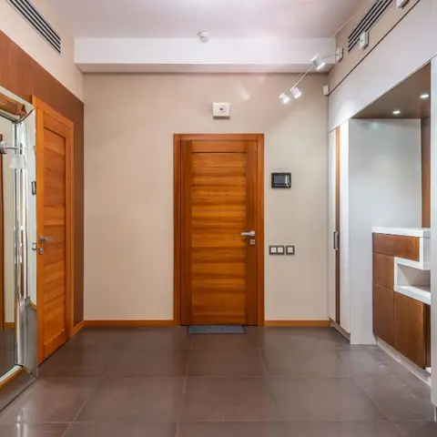 Entrance hallway with a row of matching wood-veneer doors, a full-length leaning mirror, and a built-in storage console with a lit display niche.