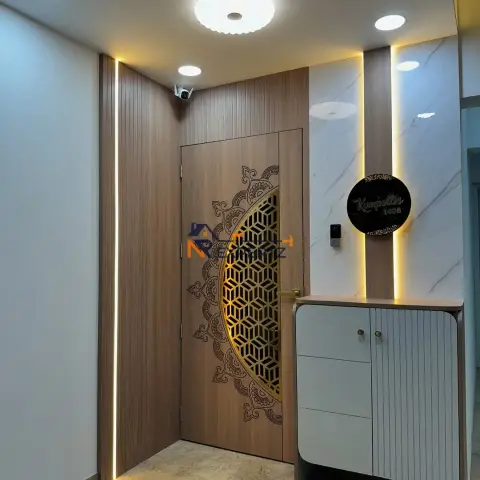 Entrance lobby with a wood-laminate main door carrying an etched mandala and a gold CNC jaali half-disc