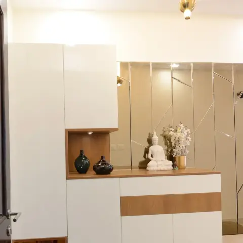 Entry console-and-storage unit in white laminate with an oak ledge, backed by bronze mirror panels in a geometric bevel layout and styled with a white Buddha