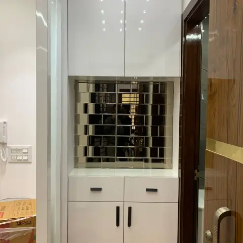 Entry console beside the main door: a white high-gloss shoe cabinet with black bar handles and a loft above, its open niche backed in bevelled mirror tiles