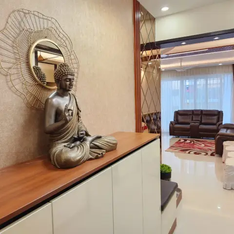 Entry console in white gloss with a teak top carrying a large bronze seated Buddha under a gold petal-burst round mirror on a textured beige wall