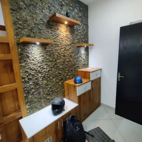 Entry corner with an olive split-face stone wall lit by three staggered wood shelves