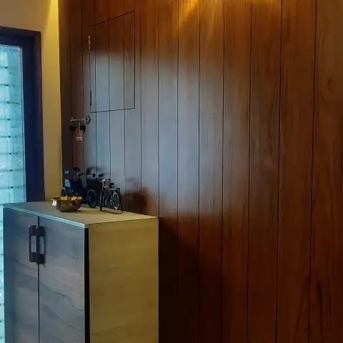 Entry foyer lined floor-to-ceiling in vertical teak veneer with a cove wash down the top edge, a butterfly-shaped acrylic LED light on the panelling