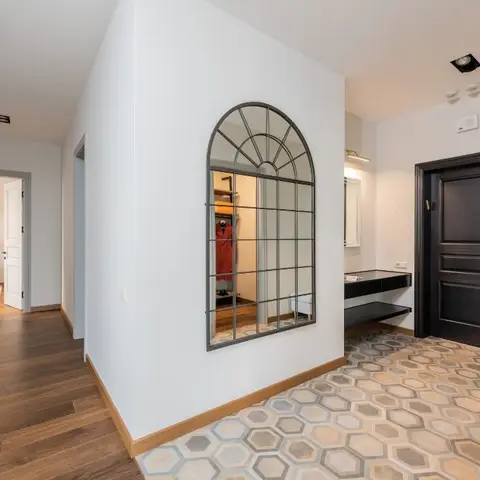 Entry foyer with a hexagon-patterned tile floor, an arched window-pane mirror over a floating black console, beside a dark wood-panelled main door.