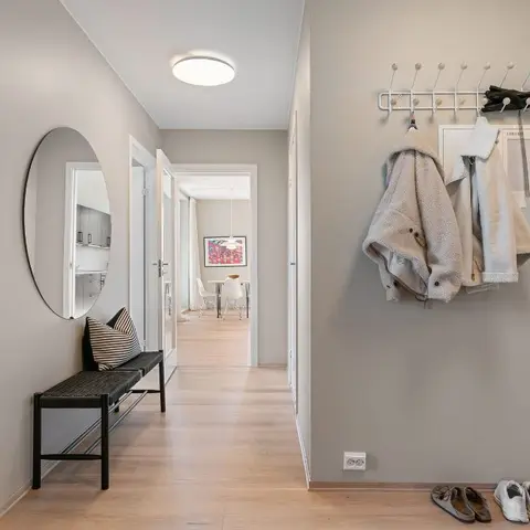 Entry foyer with a round mirror over a black bench, a wall-mounted coat rack with hanging jackets and shoes lined against the wall