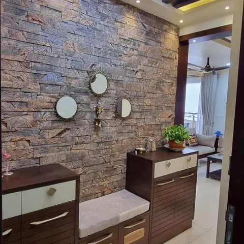 Entry foyer with a stacked-stone cladding accent wall, a cluster of three round mirrors, and a dark wood shoe cabinet with a cushioned bench seat.