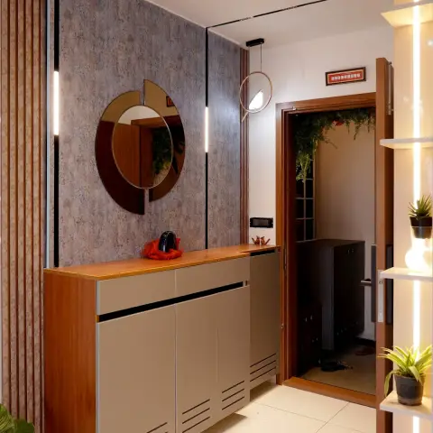 Entry foyer with a wall-hung louvred shoe cabinet under a teak top, an overlapping-disc round mirror on stone-textured wallpaper