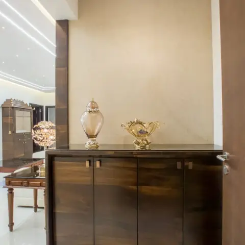 Entry foyer with a wall-hung four-shutter cabinet in dark high-gloss veneer against a beige textured wall, two amber glass urns on top