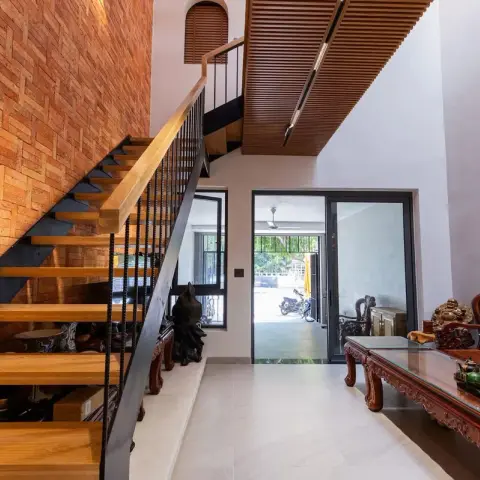 Entry hall where solid timber treads cantilever off a black steel stringer against a terracotta brick wall laid in basketweave, under a slatted wood soffit