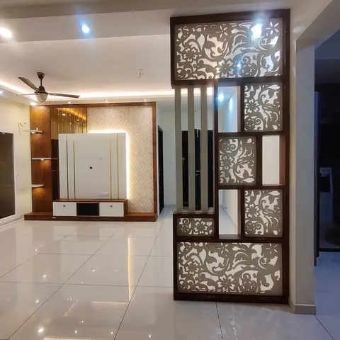Entry living space with a carved wooden jaali room divider beside a mirrored TV unit wall in hexagonal cream tile.