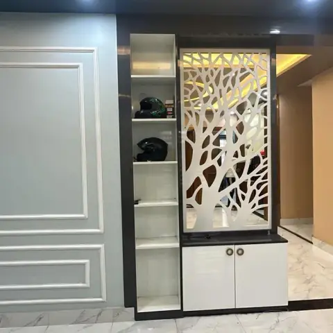 Entry lobby with a white CNC tree-branch jaali screen backlit above a two-shutter shoe cabinet, alongside a duck-egg moulded wall and a teak flush main door.