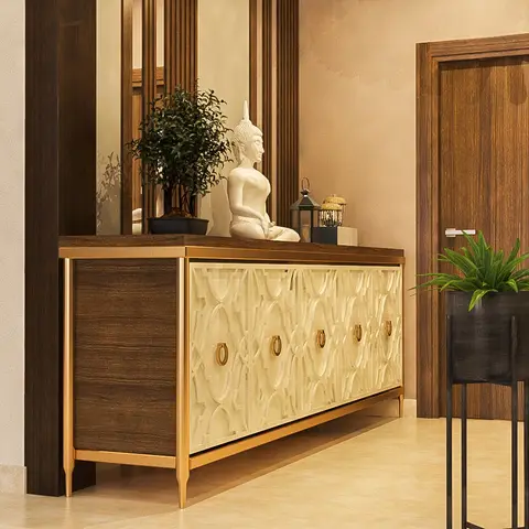 Entryway console in dark wood with gold trim and carved fretwork door panels, styled with a Buddha statue, a bonsai plant, and a fluted-frame mirror above.