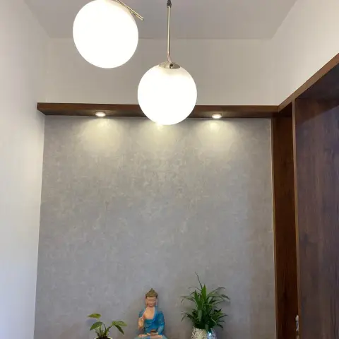 Entryway console niche with a textured wallpaper backdrop, twin globe pendant lights and a styled Buddha statue flanked by plants.