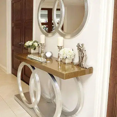 Entryway console table with an interlocking silver ring base and gold top, styled with candles, florals, and a pair of round mirrors above.