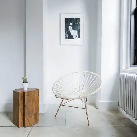 Entryway corner with a woven cord accent chair on copper-tone splayed legs, a live-edge wood side table with a small cactus