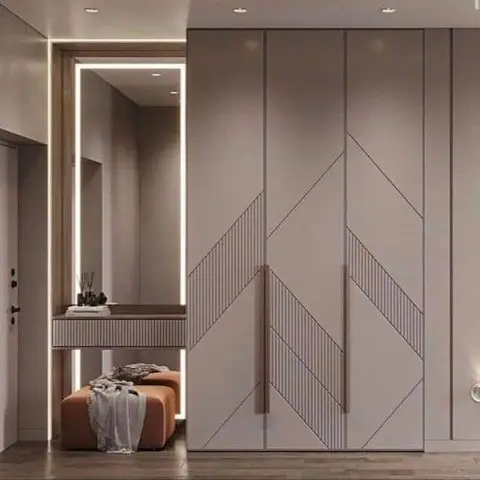 Entryway dressing nook with a full-height LED-edged mirror, a slim console, and an orange upholstered ottoman beside a geometric-panelled wardrobe wall.