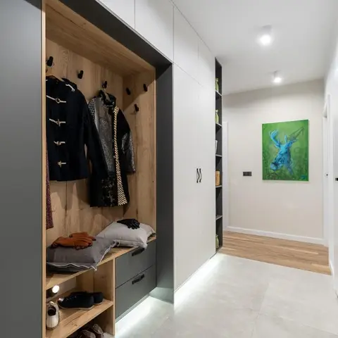 Entryway mudroom with an open wood-lined coat and shoe storage niche beside built-in grey cabinetry