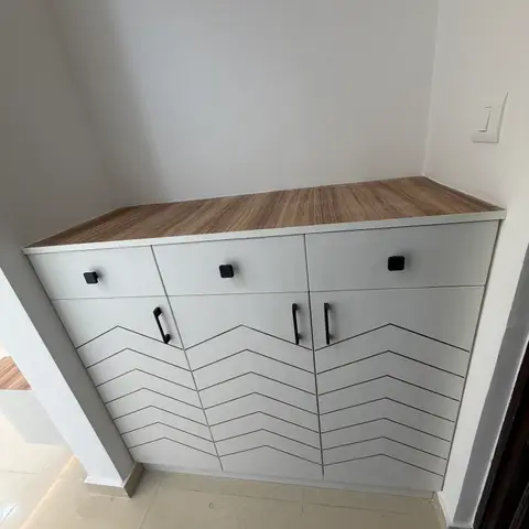 Entryway shoe cabinet with chevron-patterned white shutters and black bar handles, topped with a wood-laminate counter.