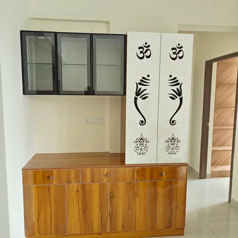 Entryway storage nook with a wood-laminate crockery unit and glass display cabinet beside a tall white pooja cupboard carved with Om and Ganesha motifs