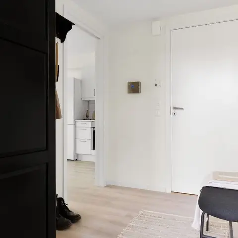 Entryway with a black panelled wardrobe, a grey upholstered stool styled with folded towels, wall hooks holding a canvas tote