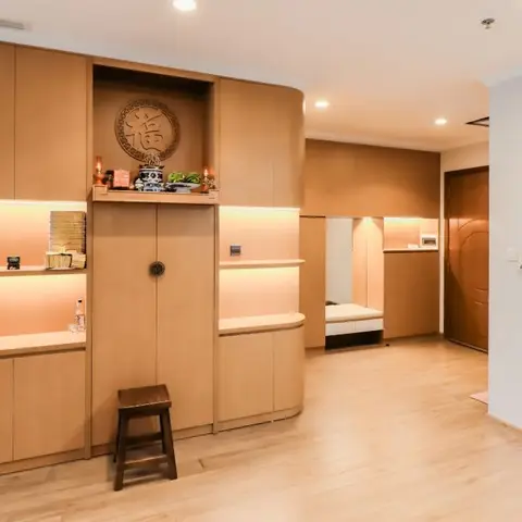 Entryway with a curved built-in wood storage and display wall with backlit niches and a carved medallion, leading past the main door.