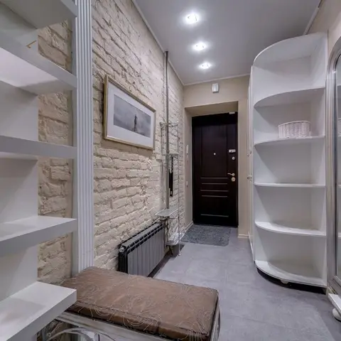 Entryway with a dark wood front door, exposed whitewashed brick wall, a curved white shelving unit and a full-length mirror.