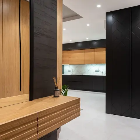 Entryway with a fluted oak console table beside a black geometric-clad wall pillar, opening into a matte black kitchen.