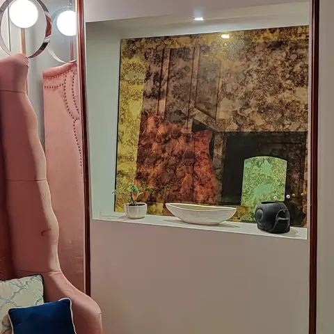 Entryway with a full-length carved wood-framed mirror beside a blush-pink tufted bench, and a lit display niche styled with an abstract art print