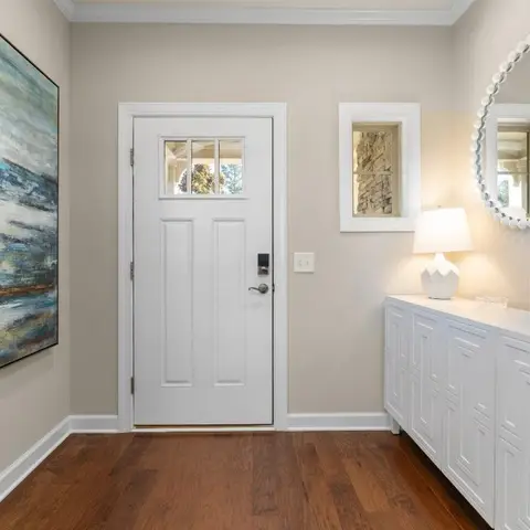 Entryway with a white panelled console table under a round beaded mirror, a large abstract blue seascape painting, a ceramic table lamp