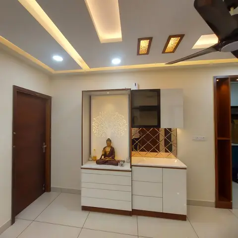 Entryway with a wooden main door beside a backlit pooja niche unit with a tree motif panel and Buddha idol, diamond-mirror splashback cabinet