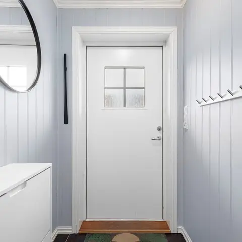 Entryway with pale blue beadboard panelling, a round mirror, wall-mounted coat hooks, and a white built-in shoe cabinet.