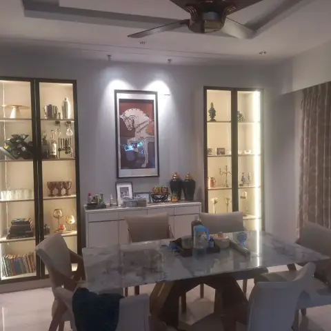 Evening dining room with two floor-to-ceiling black-framed glass display cabinets, each shelf lit