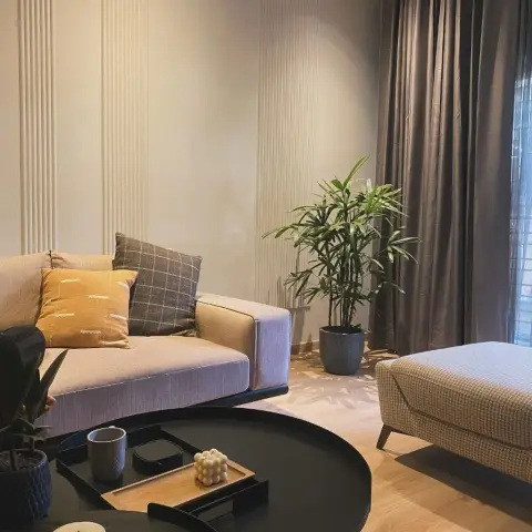 Evening light across a beige fabric sofa with a mustard and windowpane-check cushion pair, a houndstooth ottoman