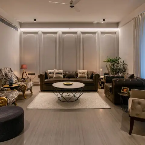 Evening living room with a backlit moulded panel wall behind twin olive-brown chesterfields, gilt-legged floral armchairs