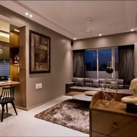 Evening shot of a compact flat where a raised wood platform with grey cushions fills the window bay, a shag rug and a Buddha-topped wood chest hold the centre
