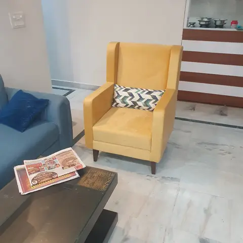 Everyday living room with a mustard wingback armchair and blue sofa around a dark wood-and-glass coffee table