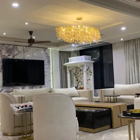 Family living room with a grey-veined marble TV wall edged by a gold backlit reveal, cream swivel tub chairs and sofas around black-and-gold nesting tables